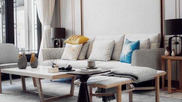 This is a photograph of an elegant contemporary living room. It features smooth white walls, a white sofa, black chairs, and a white accent wall with an interesting geometric pattern. The furniture is finished in shades of black and white, complimenting the color scheme of the room. The white sofa is set on a striking black and white patterned rug that brings texture and depth to the design. The back wall features a tall black bookcase filled with books and decorative objects, adding visual interest and character to the room. In addition, floor to ceiling windows and glass doors allow for plenty of natural