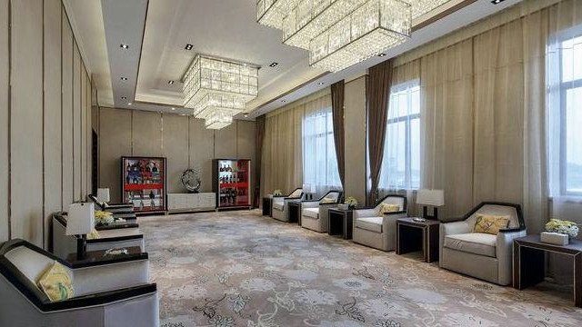 This picture shows a modern and luxuriously designed living room. The room features a large grey sofa, with several black cushions, a coffee table with a glass top, and two armchairs. The walls are white with a unique wall-art design, and the floor is covered with a grey and white patterned rug.