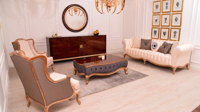 A modern lobby with a round white ceiling boasting intricate gold etchings, luxurious white leather couches, and ornately detailed walls, floors, and columns.