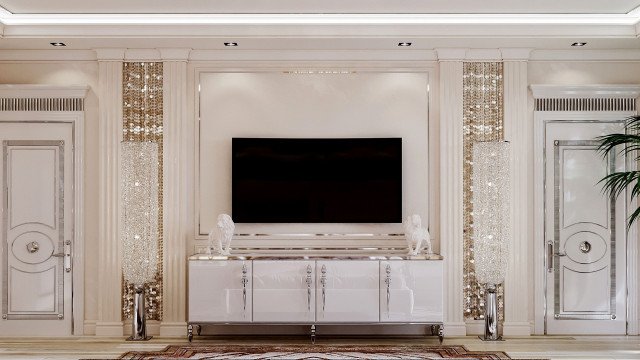 This picture shows an elegant living room from the interior design company Antonovich Design. It features a large, light blue velvet couch set against a white wall with three windows for natural light. There is a white fireplace with intricate woodworking designs set into the wall. The floor is a classic wood parquet pattern, and along the walls are white built-in shelving and cabinets. There are also two small side tables and a beautiful chandelier in the center of the room.