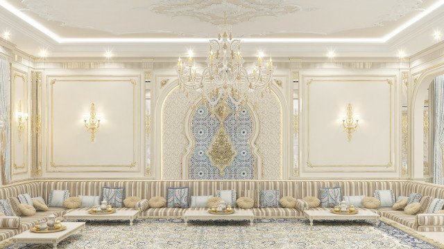 This picture shows an elegant and luxurious living room with a grand chandelier hanging from the ceiling. The walls are painted a light cream color, and there is a white marble fireplace with a gold trim in the center of the room. The floor is covered with a stunning dark wood parquetry, and there is a comfortable brown leather sofa with several patterned cushions in the corner. Two modern armchairs are placed on a white and brown rug, and there is a glass table between them. On either side of the fireplace there are tall wooden bookcases with a selection of books and