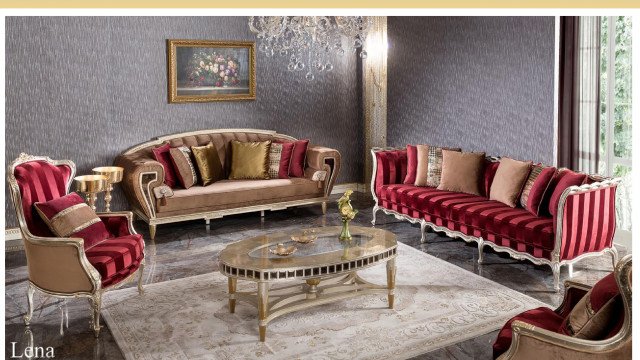 This picture shows a luxurious living room in shades of white and gold. It features an elegant white sofa, two matching armchairs, and a center table with a gold base and top. There is a large ornate mirror mounted on the wall above the sofa, and luxurious curtains framing the tall windows. A statement chandelier hangs from the ceiling, adding a touch of glamour to the space.