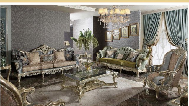 This picture shows an elegant living room with a luxurious decor. There are two comfortable grey sofas, a round ottoman in the center, and a white marble coffee table. The walls are decorated with gold framed photographs and a contemporary framed artwork. On the shelf behind the sofas there are ornate sculptures and a few books. The room is illuminated with a modern chandelier and additional lamps.
