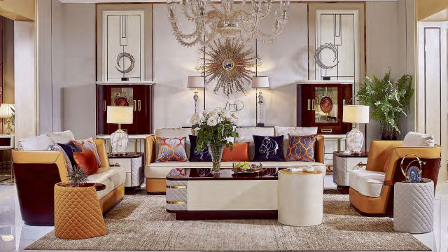 The picture shows a modern interior design featuring chic, contemporary elements. The room is decorated in shades of white, grey, and blue. The walls are covered in textured wallpaper and have large windows that allow for natural light. In the center of the room, there is a luxurious white leather sofa set with a matching white coffee table and modern cabinets for storage. On the other side of the room, there is a sleek counter top and a marble wall with built-in shelves for displaying decorative items. Overall, the room has a sophisticated, stylish feel.