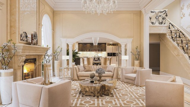 This picture shows an elegant and luxurious living room interior. It features a rich cream sofa with several pale pink pillows and a matching armchair. The walls are painted a light grey with gilded gold accents. A white and grey rug covers the floor. In the corner is a glass-topped center table with a marble base and two matching side tables. There is a gold framed wall mirror on the opposite side of the room. On the walls are two beautiful oil paintings adding to the sophisticated look of the space.