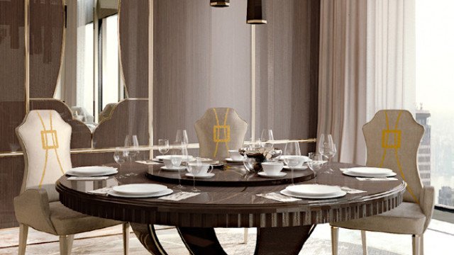 This picture is of a luxurious dining room. The walls are painted white, with illuminated recessed lighting and coffered ceilings adding a touch of glamour to the space. The large, wooden dining table is surrounded by beige velvet dining chairs, while a modern glass chandelier hangs overhead. The space also features a striking mirror-topped sideboard and a statement white sofa, complemented by a soft pink ottoman, making this a truly beautiful and inviting space for entertaining.