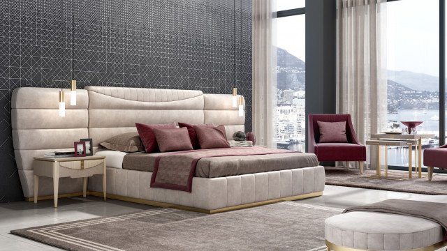 This picture is showing a modern-style bedroom with a large rectangular bed in the center. The bed appears to have a dark wood frame, with a light gray headboard and white sheets. There are two matching night stands on either side of the bed with abstract wall art on the walls. The flooring is a grayish-brown tile that goes well with the modern decor. A patterned rug is placed near the bed for warmth and comfort. The overall look is sleek and stylish with a contemporary feel.