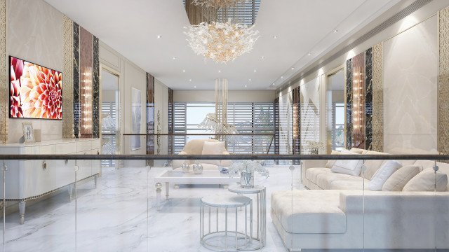 This picture is of a modern and luxurious living room featuring beige sofas and armchairs with white and navy accents. The room has arched windows encased by navy curtains, a crystal chandelier, and dark hardwood floors. A round marble coffee table rests in the center of the room, surrounded by chevron print area rugs.