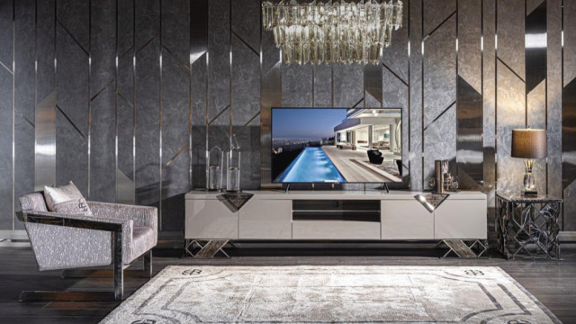 This picture shows a luxurious modern dining room. The room is decorated in an elegant and sophisticated style, with a cream and gold color scheme. The walls feature a unique textured wallpaper, and the ceiling has a beautiful geometric design. The dining table is a sleek black marble, with matching black chairs upholstered in a luxurious velvet. The room also features a stunning crystal chandelier, a glass-fronted cabinetry, and a large mirror, which helps to create an airy and spacious atmosphere.