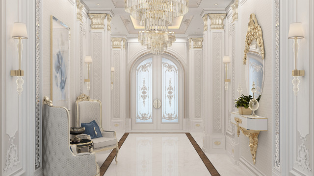 This picture shows a large and well-furnished hallway in a luxurious interior design. The walls are covered in light blue and white wallpaper with intricate detail. There is an ornate chandelier hanging from the high ceiling and a white marble flooring with gold accents. The hallway is filled with statement furniture such as an elegant tufted sofa, two armchairs, a white side table, a console table with intricate designs, and several wall art pieces. The hallway also features two windows with white curtains and a large mirror framed in gold.