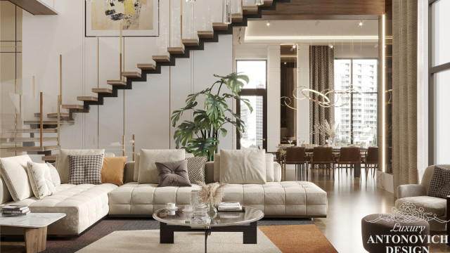 This picture shows an interior design with a modern, luxury style. The room features a stone wall with contemporary artwork, a built-in bookshelf, and a large comfortable couch in a grey upholstery. A glass coffee table is surrounded by a mix of cushioned armchairs and modern poufs, providing seating for the room. A fur rug allows for warmth and comfort, and warm, inviting lighting creates a cozy atmosphere.
