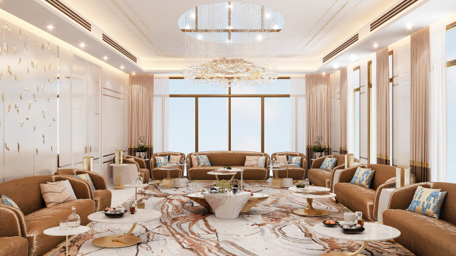 This picture shows a luxurious living room with a modern interior design. It features a white leather sectional couch and comfortable armchairs facing a large, stone fireplace. The walls are ornately decorated with gold accents, and the room is illuminated by recessed ceiling lights and tall standing lamps. The floor is covered with a plush grey rug, and the room has lovely beige drapes hung from an arched ceiling.