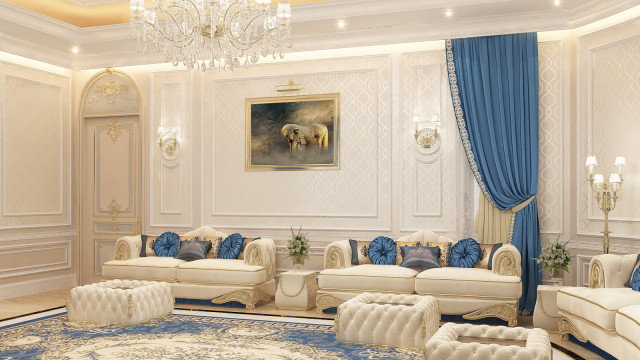 This picture shows an interior design of a luxurious living room. The room features a large cream-colored sofa with golden detailing and two matching armchairs. A large crystal chandelier hangs from the ceiling, giving off a soft light that illuminates the warmly-colored walls. On the walls are two beautiful paintings and several pieces of furniture, including a console table and a large coffee table. The room is completed with a neutral toned rug, adding texture and color to the room.
