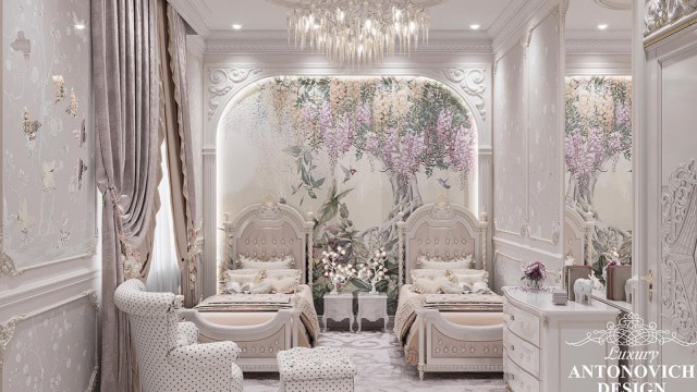 This picture shows a luxurious interior design with a white leather loveseat, two marble end tables, and matching white lamps. The walls are adorned with an elegant dark wood paneling and an intricately patterned light pink and white wallpaper. There is also a large fireplace mantel with a decorative mirror above it. Overall, the room has a very luxurious and sophisticated feel.
