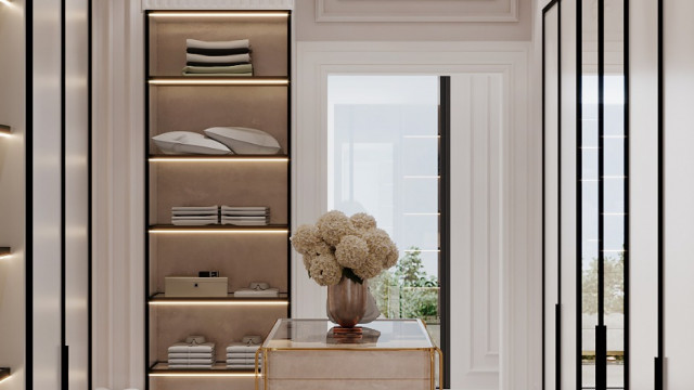 This image is of an elegantly designed and decorated library. The room has walls lined with dark wooden bookshelves, a pair of armchairs upholstered in white fabric, and patterned rugs on the floor. A large window offers natural light and a cozy atmosphere. The center of the room holds a grand chandelier hung above a large oak desk complete with a green lamp and other decorative accessories. The room has a modern but timeless feel that would make any reader feel right at home.