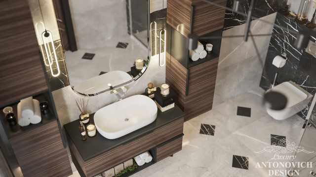 This picture depicts a luxurious bathroom space with a floating vanity made of marble and a large decorative mirror behind it. There are two sinks set into the vanity with separate faucets, and a wall-mounted towel rack on the right side. The walls are tiled with a white and cream pattern, with darker accents in some tile pieces. The countertop has a built-in storage system with multiple drawers, and a large shower is visible in the background with a glass door.