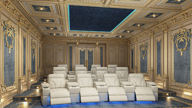 This picture shows a luxurious living room with an elegant white and gold color scheme. The room features an ornate white couch with gold accents, a large round ottoman in the middle, and two classic armchairs to the side. The ornate fireplace is covered in marble and gold accents, while the wall is adorned with a unique gold-framed mirror. The space is flooded with natural light from the large bay windows which lead out to a balcony view.