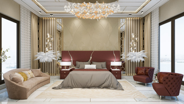 This picture shows a modern living room in a luxurious home, featuring a large sofa upholstered in white with several vibrant patterned cushions, two end tables, and an ornate rose gold chandelier. There are two armchairs in the foreground, one of which is grey and the other has a light beige velvet upholstery. The ceiling features intricate crown moulding, recessed lighting fixtures, and a bright white paint. The floor is hardwood and there is a shaggy ivory rug in the center.