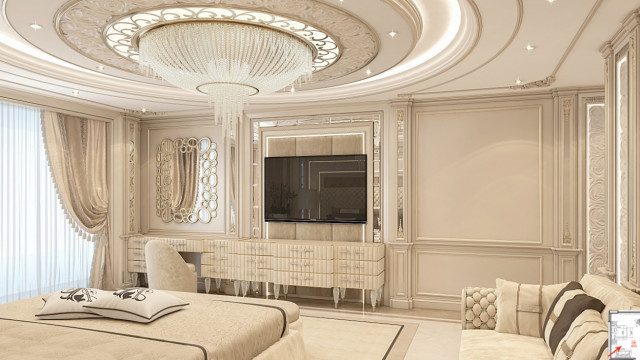 This is an image of a modern-style bedroom designed by Antonovich Design. It features a grand king-size bed with white pillows and gold embroidery, framed by two rose-gold mirrored nightstands. The walls are painted in a cream color and feature elegant scrollwork. In the corner sits a plush velvet armchair and ottoman, and the floor is adorned with a large white-and-gold shag rug. Windows covered with white gauzy curtains let in natural light, while the ceiling boasts a large crystal chandelier.