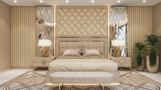 This picture shows a luxurious bedroom designed by Antonovich Design. The bedroom features decor in shades of ivory and gold, with a richly patterned carpet, golden wall sconces, and a luxurious velvet headboard. The walls are adorned with a grand mirror and artwork, while the bed is dressed in plush bedding.