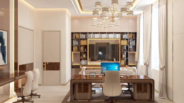 This picture shows a luxurious, modern living room. The walls are white and decorated with golden accents and artwork. The furniture is upholstered in gray, giving the space a sleek and sophisticated look. The center of the room features a large, round ottoman with velvet upholstery, surrounded by two armchairs. A small side table with a glass top holds a lamp and other decorative items. The white curtains on the large windows provide an airy feel to the room, while a large crystal chandelier hangs above the ottoman, adding opulence and glamour