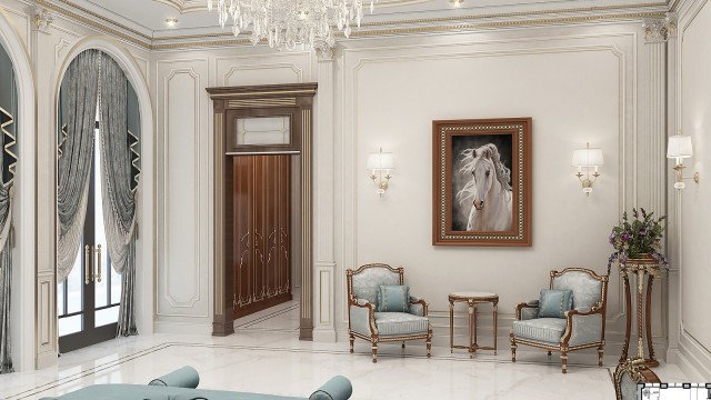 This picture shows a luxurious bedroom suite with two chairs and a loveseat upholstered in a cream and beige fabric. The walls are painted a deep beige color, and the floor is covered in a light cream carpet. A richly decorated bedframe sits in the center of the room, with a matching nightstand beside it. A large framed mirror hangs on the wall above the bed, and light fixtures adorn either side of the mirror. On the opposite wall is a window covered with cream curtains, and floor-to-ceiling built-in shelves contain decorative