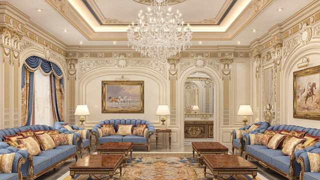 This picture shows an elegant and luxurious living area. The walls are decorated with ornate molding and paneling, a large chandelier hangs from the ceiling, and the floors are covered in beige carpet. In the center of the room is a white sofa with plush pillows, while two chairs sit in front of it. A deco-style coffee table and side table are placed in the room, surrounded by a variety of decorative pieces such as vases, urns, and sculptures. Luxury curtains hang from the windows and a lush indoor plant sits in one corner
