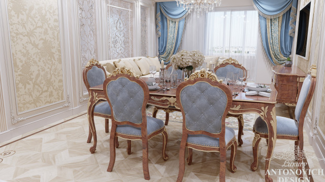 This picture shows an elegant modern living room designed by Antonovich Design. It features a beige velvet sofa and armchairs, a glass top coffee table, a white lacquer console table, dark wood flooring, and a large abstract painting hung on the wall. The room is bright and airy, with lots of natural light coming in through the windows.