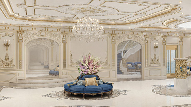 This picture shows an elegant living room with two large navy-blue couches facing each other. The walls are a pale yellow color, and the floor is covered in a light-colored rug with diamond patterns. There is a beige armchair in the corner, and a large wooden coffee table in the center. An intricate gold chandelier hangs from the ceiling, and several house plants dot the area. The room has large windows that let in natural light, and sheer white curtains allow some privacy while still letting in light.
