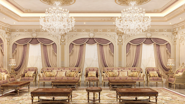 jpgThe picture shows an elegantly decorated living room with a stylishly upholstered sofa and two matching armchairs. The seating area is centered around an ornate coffee table with an intricate, golden base. The walls are painted in a warm neutral color, while the curtains, carpets, and accessories bring in bright, vibrant colors and patterns to the overall space. There is a television mounted in one corner of the room and tall shelves filled with books and decorative elements on the other side.