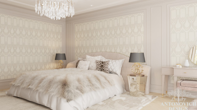 This picture shows a stunning modern bedroom with a high-end interior design. The room has a black and white color theme, with a luxurious upholstered king-size bed against one wall. A crystal chandelier hangs above the bed, adding a touch of elegance to the space. On the opposite wall, there is a floor-to-ceiling window that lets in plenty of natural light. In the middle of the room, there is an elegant white vanity with a padded bench. Adding a bit of color to the room are the two gold-framed mirrors that
