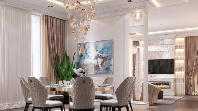 This picture is of a luxurious living room decorated with modern and classic elements. The focal point of the room is a large, white sofa that is set in front of a contemporary fireplace. On either side of the sofa are two ornate chairs upholstered in a light tan fabric. The walls of the room are painted a dove grey and have gold accents. On one wall is a large flat-screen television that is mounted to the wall and framed with an ornate gold mirror. The room also features several lush plants, a modern chandelier, and a wooden accent table with