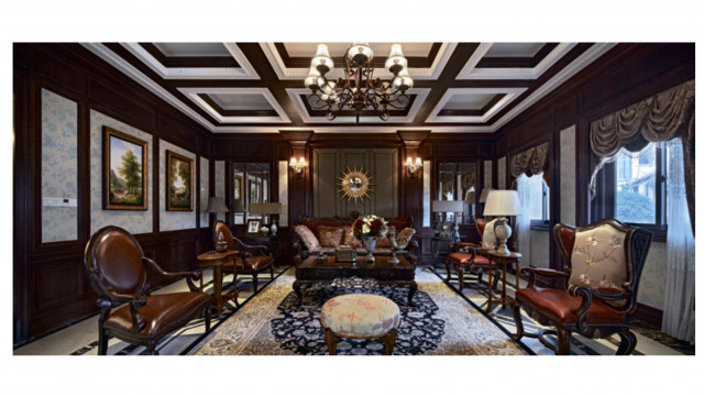 This picture shows a luxurious bedroom interior with dark walls and gleaming gold accents. It features a large, regal bed with a plush, tufted headboard and large pillows. Along the wall is a large, vintage-style mirror framed by golden ornate carvings. A metal chandelier hangs from the ceiling, adding elegance and sophistication to the space. The floor is decorated in chevron-style tiles, and there are two armchairs in the corner of the room.