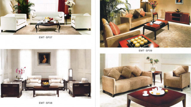 This picture shows a modern, luxurious living room with cream walls, white furniture, and gold accents. The focal point is the large, white tufted sofa with a matching set of armchairs and a round glass-top coffee table in the center. The floor is a light wood, with a plush cream and gold area rug layered over the top. The walls feature several framed art pieces, and there is a round crystal chandelier hanging from the ceiling. There are two large windows that let in plenty of natural lighting, and two tall houseplants add a touch of greenery