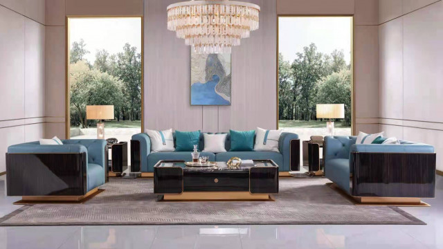 This picture is of a stylish and modern living room designed by Antonovich Design. It features a large floor-to-ceiling window, two tan leather sofas with decorative accent pillows and two cushioned armchairs in blue, white and yellow. There is also a round glass coffee table and two different patterned rugs on either side of the room. The entire space is finished with light wood trim and flooring, as well as plenty of natural light to make it look welcoming and inviting.