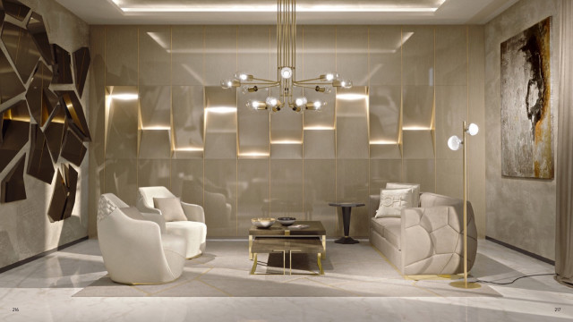 This picture shows an array of modern, luxurious furniture in a large and sophisticated living space. The living area includes an intricately patterned cream-colored sofa, two matching armchairs, a center table, and stacks of gold-accented pillows, all with a grey and black accent wall. There is also a large white furry area rug, a pair of modern glass coffee tables, and sleek floating shelves filled with books. To top it off, the room is illuminated by a grand crystal chandelier.