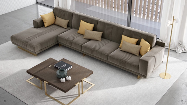 This picture shows a modernized living room with neutral floors and walls. The room has a contemporary feel, with large windows to allow natural light to enter. The focal point of this room is the tan-colored sofa and its bold geometric patterned throw pillows, adding a touch of personality to the otherwise minimalist room. The coffee table and ottoman are wood and white in finish, while two armchairs in white upholstery provide additional seating. A colorful abstract painting hangs over the sofa, providing a splash of color.