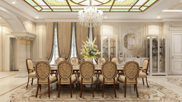 This picture shows a luxurious modern living room with a built-in marble bar area. The bar features a light brown marble countertop, a black vessel sink, and gold-colored industrial-style fixtures. There is also a white floating shelf featuring several glass jars filled with various liquors. The walls of the room feature a light beige color with a large white panoramic window as the centerpiece. The room is decorated with several vases and sculptures made from different materials.