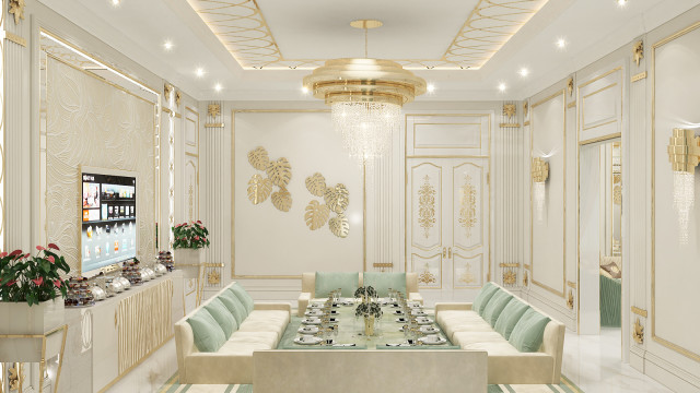 The picture shows an elaborately designed room, featuring a gray and white curved sofa, a round coffee table with a gold inlay, two metallic armchairs, a luxurious chandelier and classical columns.