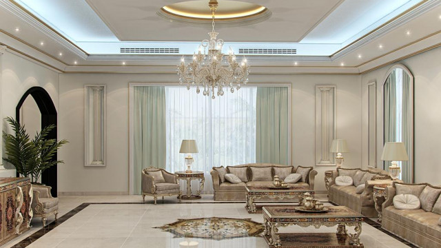 This picture shows the interior of a luxurious living room. The room has classic elegance with a modern touch. The walls are painted a light gray color, and the floor is white marble tile. In the center of the room is an elegant white sofa with gold-accented ornate arms. On one wall is an abstract painting with bright colors while the other wall has an intricate gold mirror. The room also features several floral arrangements and a large area rug with a floral pattern.