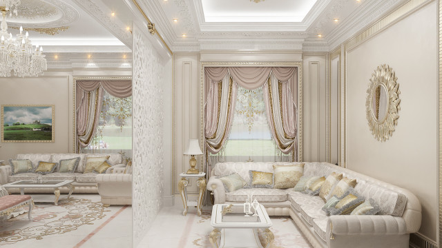 The picture shows an ornate, contemporary living room interior design. The walls are painted in a light beige color, with intricate black and gold wall coverings. A large luxury sofa is seated in the center surrounded by two polished gold end tables and two bright white armchairs. On the walls are two large art pieces framed in gold and oil paintings in between them. The floor is covered with a luxurious ivory carpet. The whole room is lit up with small recessed lighting.