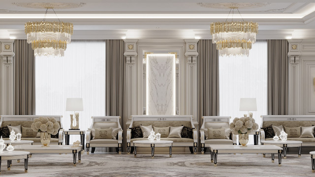 This picture shows a spacious luxury living room designed by Antonovich Design. The room is decorated with elegant white furniture and walls, complete with an ornate marble fireplace and large gilded mirror. The floor is covered in a rich, dark hardwood with a light grey and beige patterned area rug. Additionally, the room is filled with plush throw pillows and ornamental plants for a warm, inviting atmosphere.