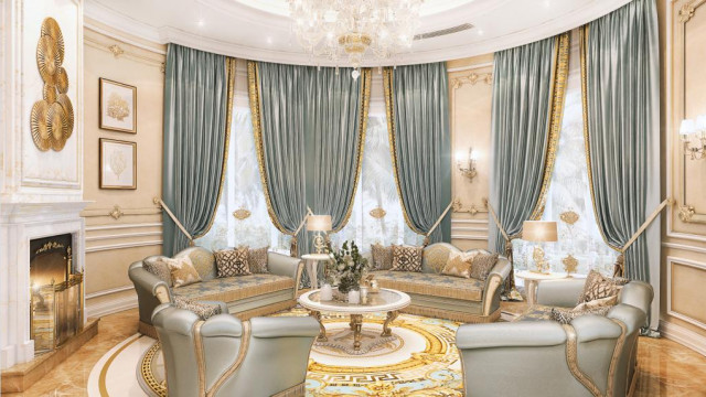 This picture shows a luxurious living room with a taupe sectional sofa and four blue accent chairs gathered around a black coffee table. There is a large, crystal chandelier hung from the ceiling, and a decorative rug in shades of gold, beige, and white creating a warm ambience. The walls are painted in a light grey tone, and large ornate mirrors are hung to create an elegant, sophisticated atmosphere.