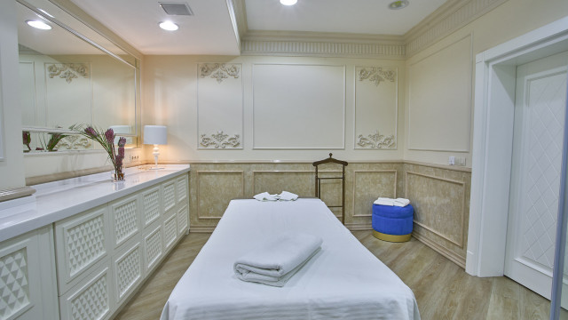 This picture shows a luxurious bathroom with a modern style. The walls are covered in white marble tile, and the floor is finished in black and white geometric patterned tiles. The vanity has a double sink and marble countertop. There is a large window above the tub which looks out onto a garden. There are also two recessed lights on the ceiling and a light sconce on the wall next to the entryway.