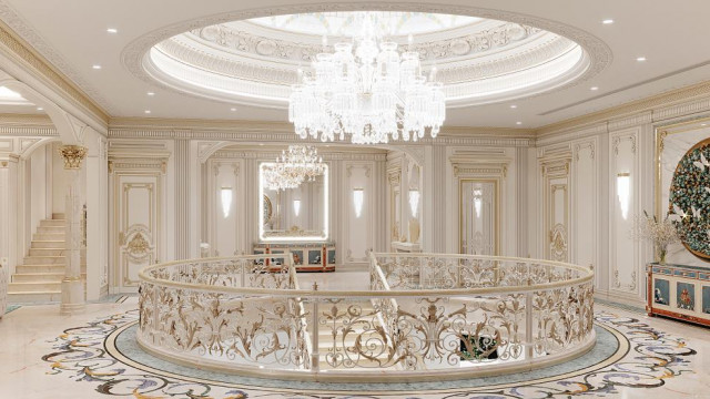 This picture shows an ornate and luxurious entryway featuring a large wooden door with intricate details and hardware, a set of stairs crafted from white marble, and a grand chandelier hanging from the ceiling. The walls are a light beige color, and there is a white balustrade atop the stairs.