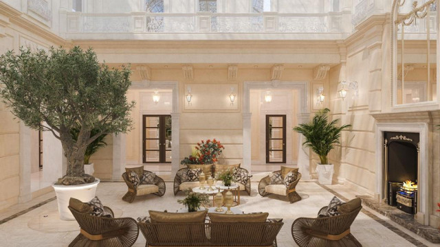 This picture shows a luxurious home interior with an elegant curved staircase. The staircase is white marble with black iron banisters and borders, which match the black iron railings of the upper level balconies. The walls and ceiling are decorated with intricate gold-colored accents, giving the interior an opulent look. The floor is made of dark wood and is topped with a large Persian rug. Luxurious furniture with velvet upholstery can be seen in the background, as well as a grand piano at the back.