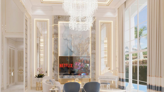 This image shows an interior design featuring a modern living room with a white leather sectional sofa, a glass coffee table, and a rug on the floor. The walls are white with a grey accent wall that has built-in shelving and a modern light fixture. There is a large window to the left of the room, which lets in plenty of natural light.