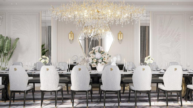 This is a picture of a luxurious living room with an ornate white marble floor and beautiful golden accents. The walls are a soft shade of beige and accented with two large paintings on either side of the light-colored sofa. The room also features an elegant chandelier above the sofa, and on the wall to the right, a stone fireplace which is surrounded by gold-colored metal panels. Finally, the room is decorated with two luxurious armchairs in a matching gold pattern and two small round tables for convenience.