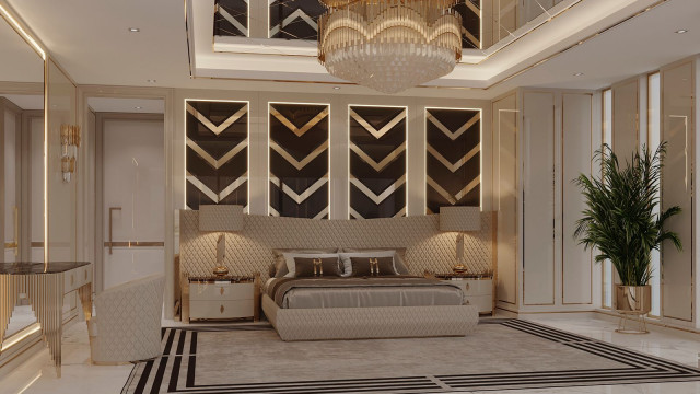 This picture shows a luxury living room designed by Antonovich Design. The room features a modern yet elegant décor in shades of gray, black, and cream. A large gray sectional sofa with ornate patterned pillows sits in the center of the room, surrounded by a black and white rug. The walls are decorated with luxurious artworks and pictures, along with black and gold shelves for storage. An ornate white chandelier hangs from the ceiling, adding a touch of grandeur to the room.