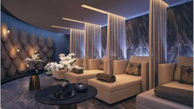 This picture shows a luxurious modern living room with a beautiful balcony view. The room features an elegant white sofa, two white sheer curtains framing the view, and a glossy textured coffee table. There is also a round white rug, a matching armchair, a floor lamp, and a painting on the wall. The walls are adorned with a patterned wallpaper, which adds to the room's unique intricacy.